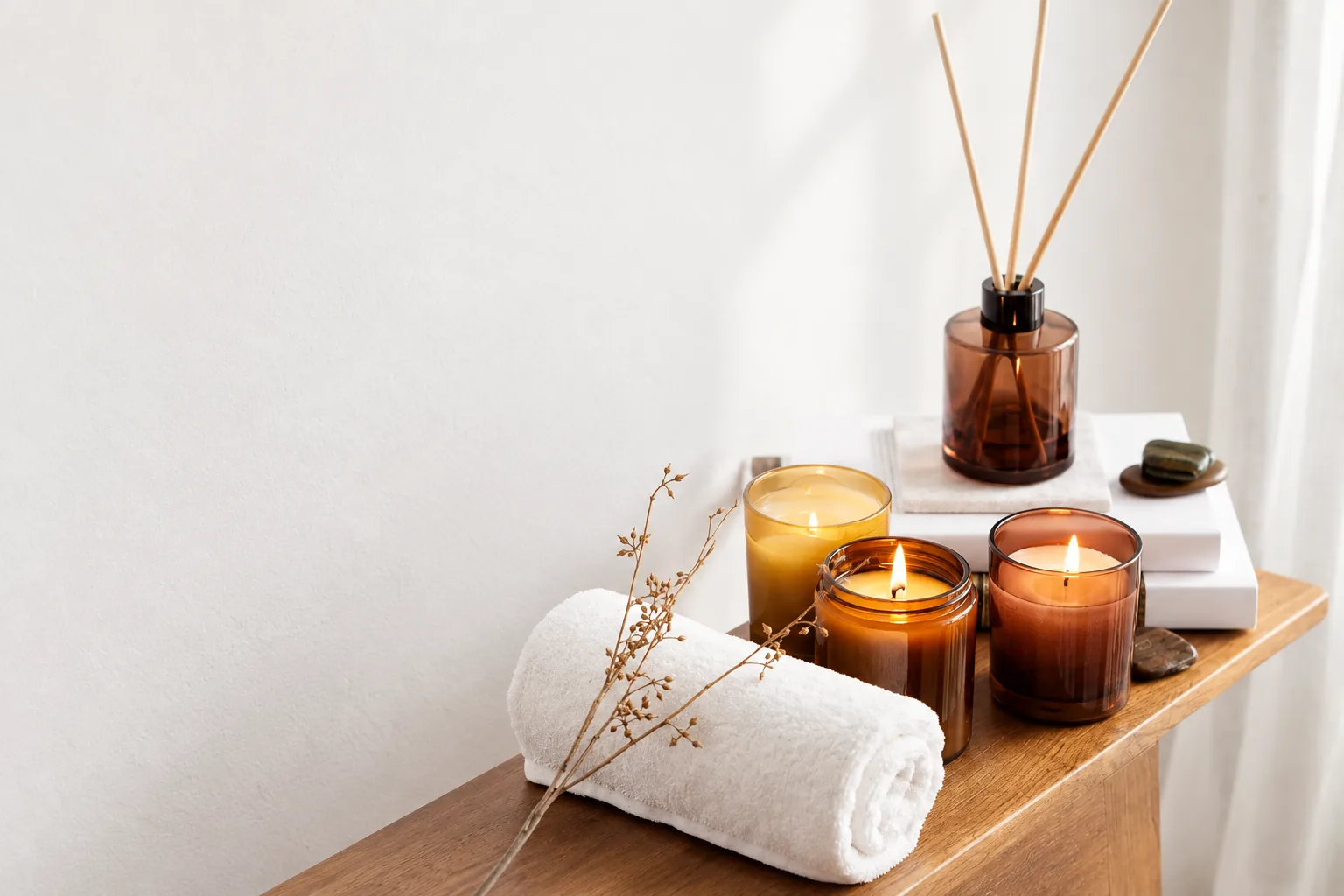 Velas encendidas, un difusor de aromas y una toalla blanca doblada sobre una mesa de madera
