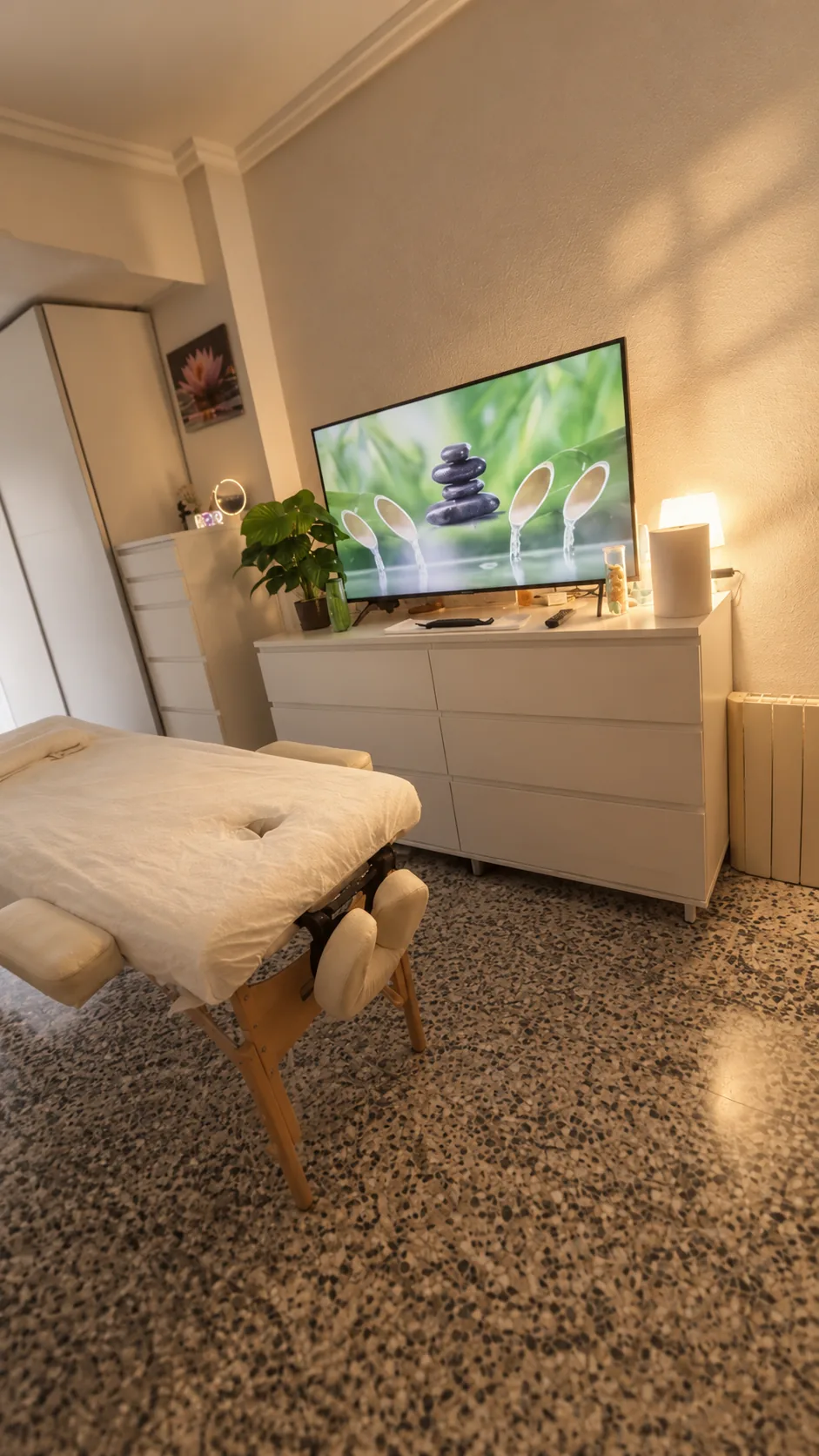Sala de masaje con camilla, televisor con imágenes de relajación y luz cálida